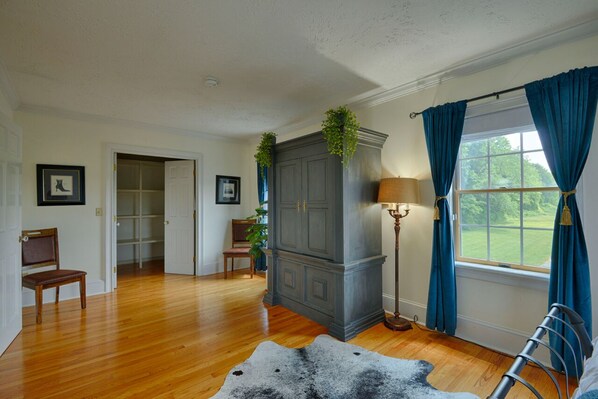 A room with hardwood flooring, a grey cabinet with plants, a lamp, a window with blue curtains, and a door leading to another room. - Hilltop Retreat -10% 5 nights or more (Auto Applies) thru 2026 (Tully)