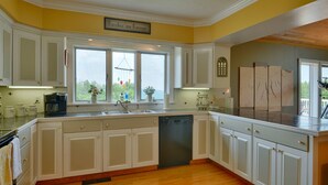Cucina con mobili bianchi, lavastoviglie, macchina da caffè e finestra vista verde.