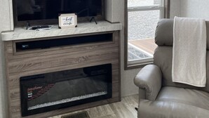 Uma sala de estar moderna com televisão de tela plana sobre um móvel de madeira, um sofá de couro confortável e vista para um corpo de água pela janela.
