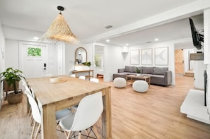 A modern living room with a wooden dining table, white chairs, a grey sofa, and a hanging light fixture. - New Modern Waterfront Bungalow Retreat 
+ Tropical Vibes + Fishing Paradise! (Melbourne)
