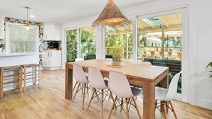 A modern kitchen with a wooden dining table, white chairs, and a hanging light fixture.