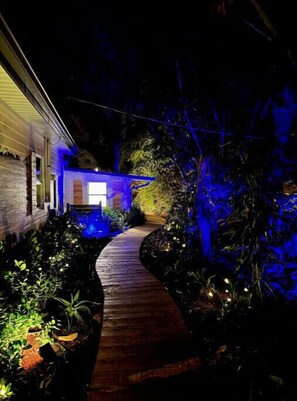 A pathway leading to a house with a blue-lit exterior and a wooden deck. - New Modern Waterfront Bungalow Retreat 
+ Tropical Vibes + Fishing Paradise! (Melbourne)