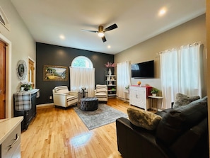 A living room with a fireplace, a ceiling fan, a TV, and a window with curtains.