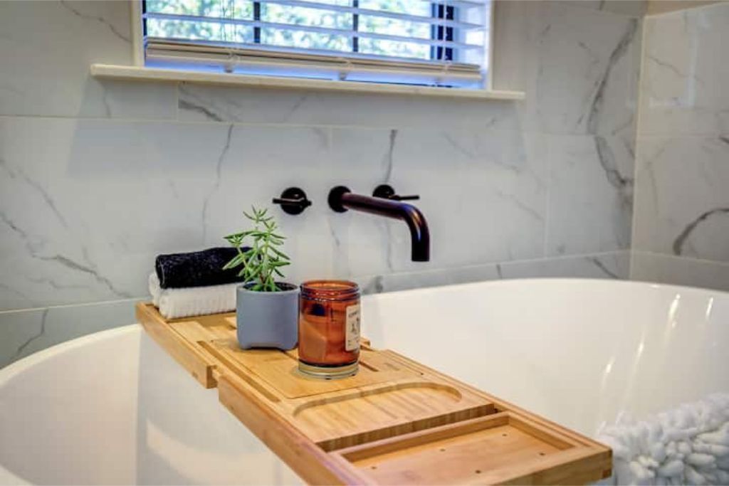 Ein Badezimmer mit einer weißen Badewanne, einem Holztablett, einer Topfpflanze und einer Kerze.