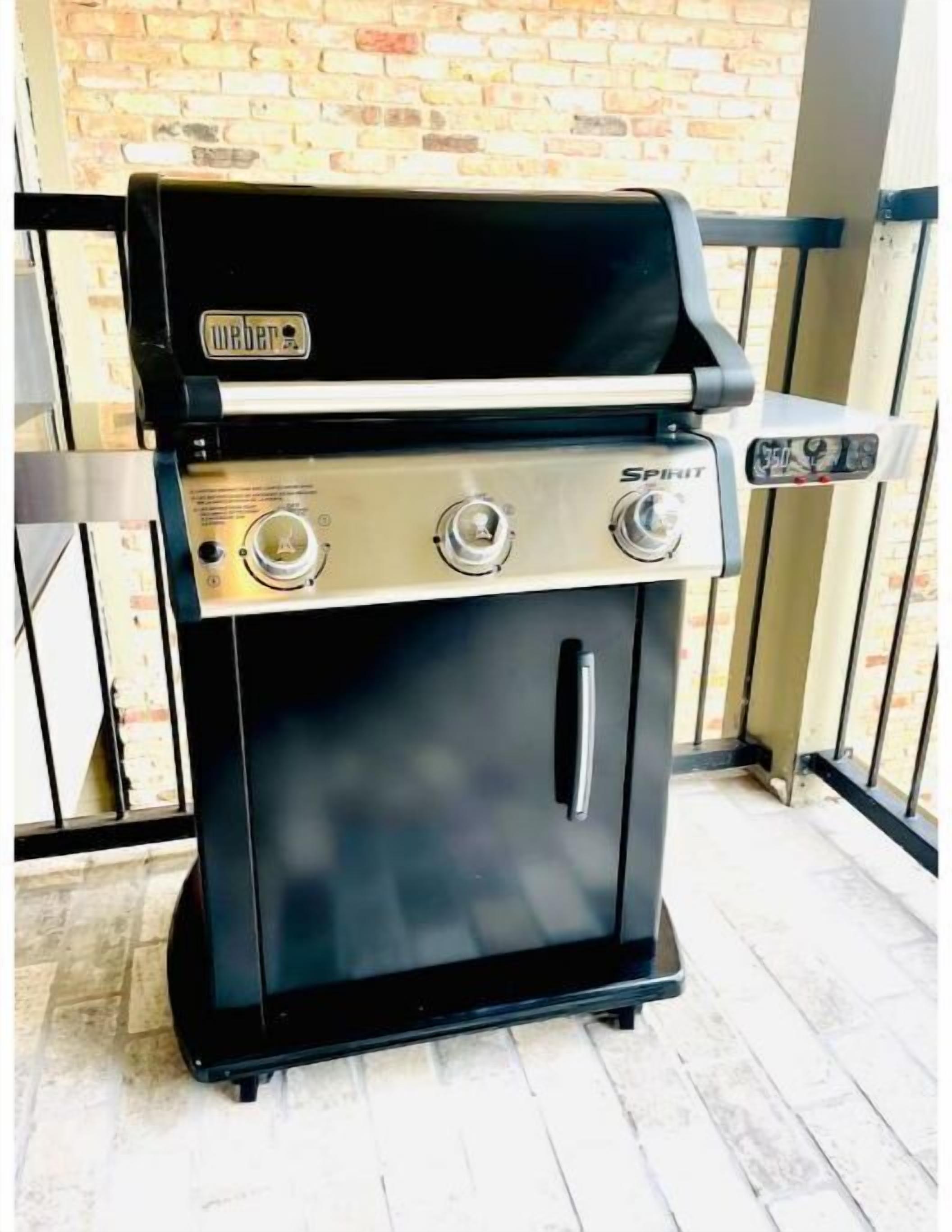A Weber Spirit grill with three control knobs, a digital display, and a black finish, set against a brick wall.