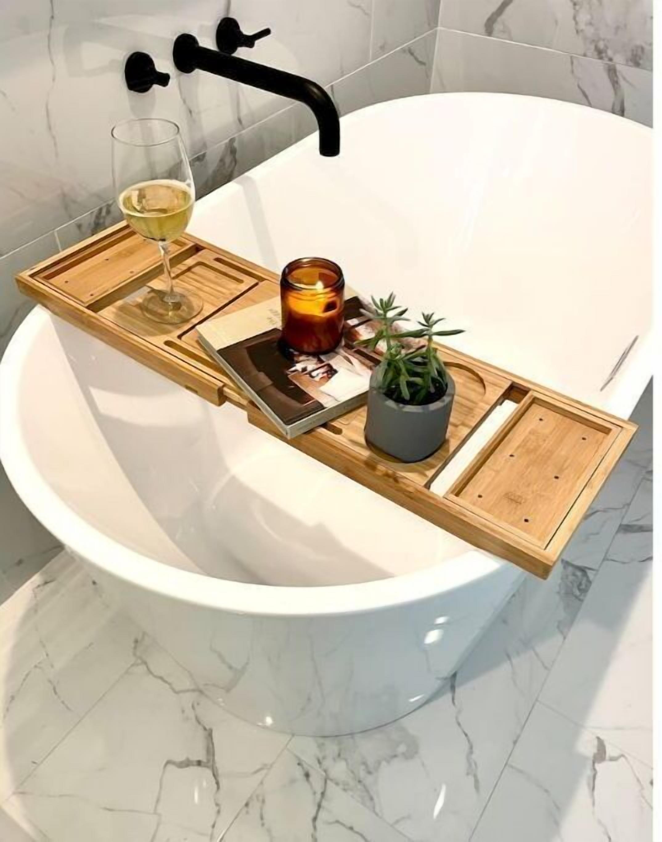 A bathtub with a wooden tray holding a glass of wine, a candle, and a small potted plant.