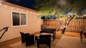 Un espace extérieur aménagé en terrasse, avec des meubles en osier, des guirlandes lumineuses et une clôture en bois.