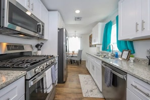 A modern kitchen with white cabinets, stainless steel appliances, a granite countertop, and a view into the dining area.