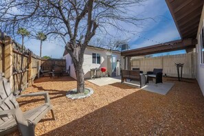 A backyard with a patio, a tree, and a wooden fence.
