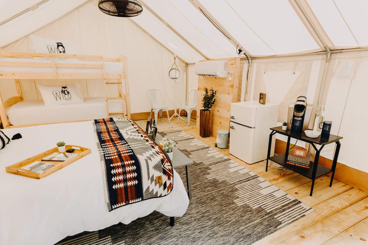 A tented accommodation with a bunk bed, a small kitchenette, a table with a plant, and a heater.