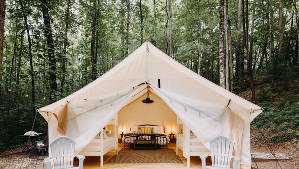 Una tienda de campaña con una cama y dos sillas en un bosque.