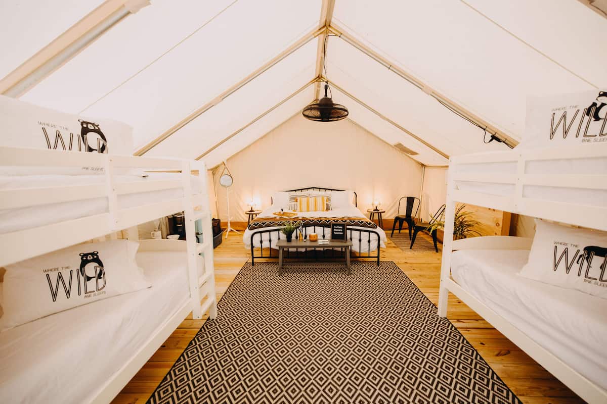 A tented accommodation with bunk beds, a central bed, and a patterned rug.