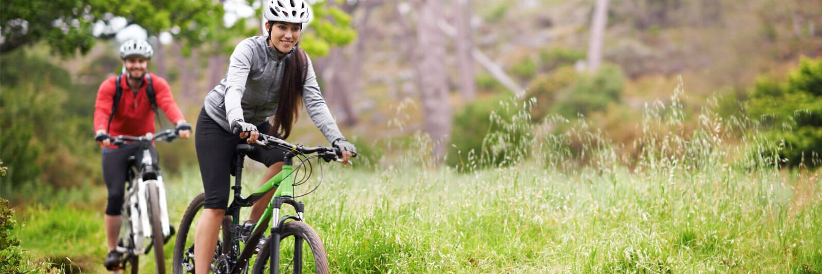 Two cyclists on a trail with natural scenery in the background.