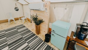 Una habitación compacta con piso de madera, un tapete a rayas blanco y negro, un refrigerador azul claro, una pequeña mesa con una cafetera y una planta en maceta.