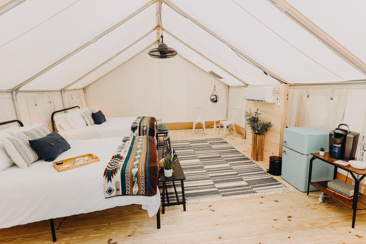A tented accommodation with a bed, a small table, a chair, a refrigerator, and a heater.