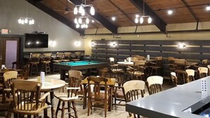 Un espacio interior amplio con varias mesas y sillas, una mesa de billar y lámparas colgantes.