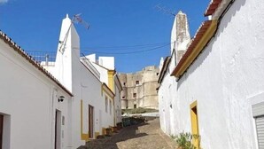 Una stretta strada acciottolata, fiancheggiata da edifici bianchi con tocchi di giallo e tetti in tegole rosse.