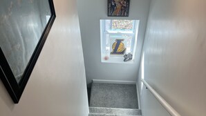 Eine Treppe mit Teppichstufen, einer Handläufe, einem gerahmten Bild auf der linken Seite und einem Fenster mit einem großen 'L'-Emblem und einem Basketball auf der rechten Seite.