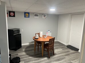 Una habitación pequeña con una mesa redonda de madera, dos sillas, un refrigerador negro, un microondas y una puerta con timbre blanco.