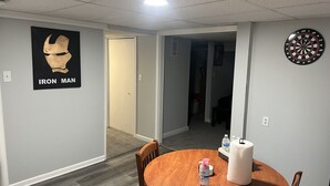 Ein Zimmer mit einem Holztisch, einem Iron Man Poster, einer Dartscheibe und einer Tür zu einem weiteren Raum.