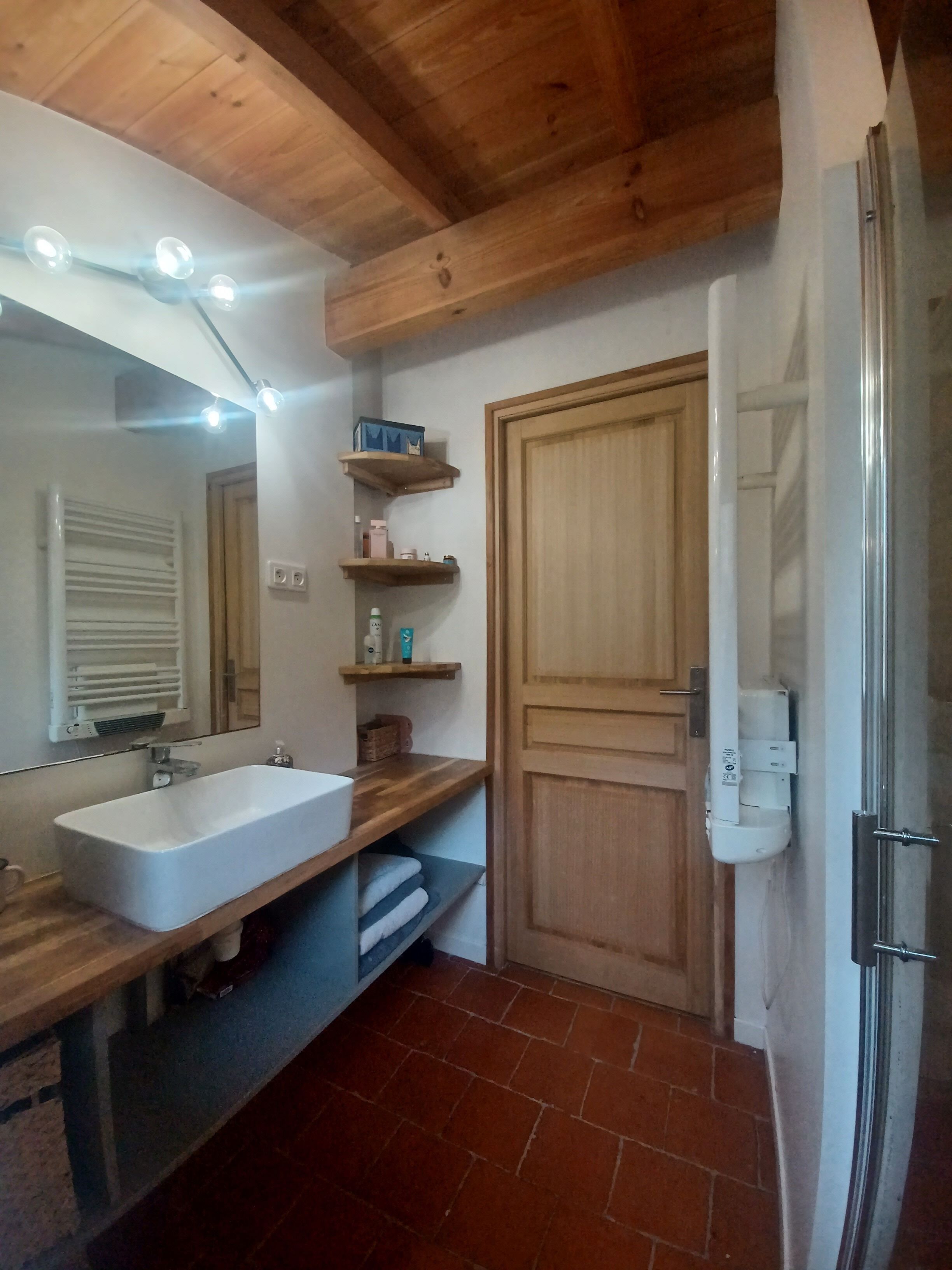 A bathroom with a wooden ceiling, a white sink, a mirror, and a shower area.