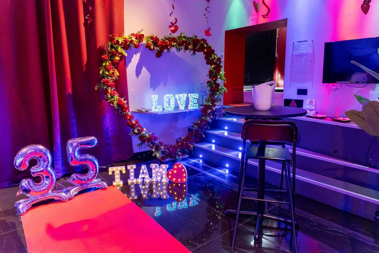 Een kamer met een bloemarrangement in hartvorm, een bord met '35 TIA' en een bord met 'LOVE'.
