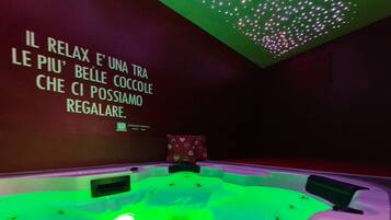 A spa room with a green-lit hot tub, a wall with text in Italian, and a ceiling with a light pattern.