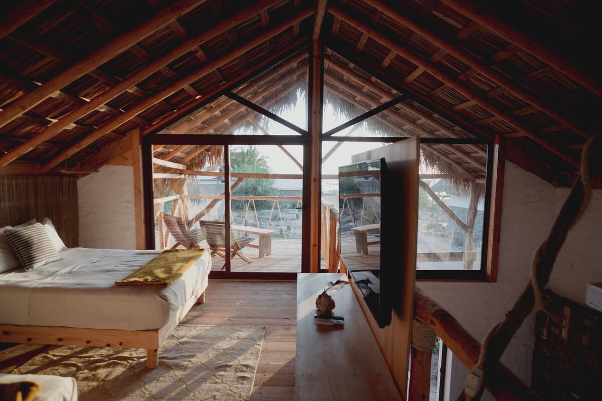 Un dormitorio acogedor con techo de madera, una cama grande, un escritorio de madera y vistas al exterior a través de amplios ventanales.