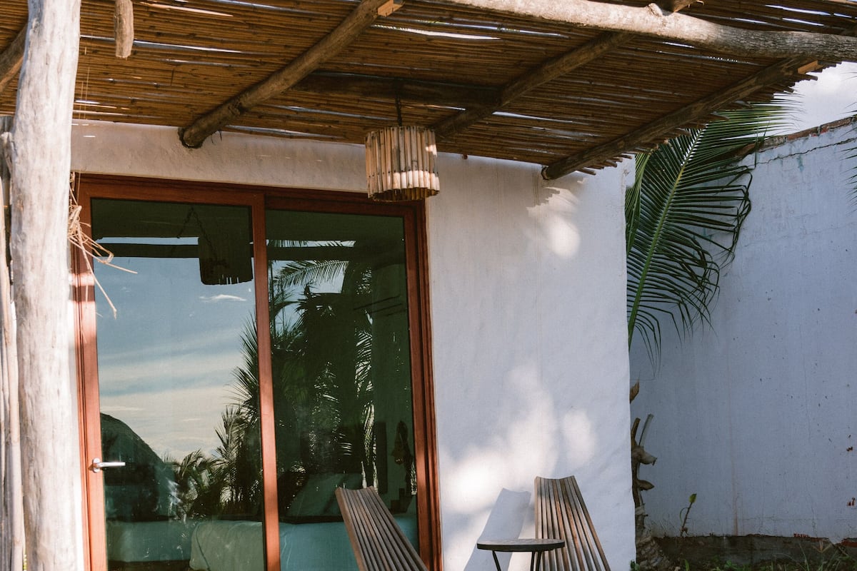 Una terraza de madera con dos sillas y una mesa, que conduce a una puerta de vidrio.