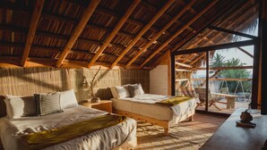 A rustic bedroom with two beds, wooden beams, a large window, and a view of palm trees. - Toninas México (Elota)