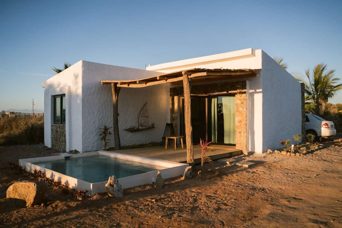 Una casa moderna con piscina, una pérgola y un coche aparcado cerca.