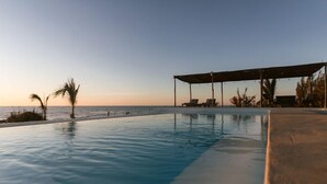 An infinity pool with a view of the ocean at sunset, lounge chairs, and a covered seating area. - Toninas México (Elota)