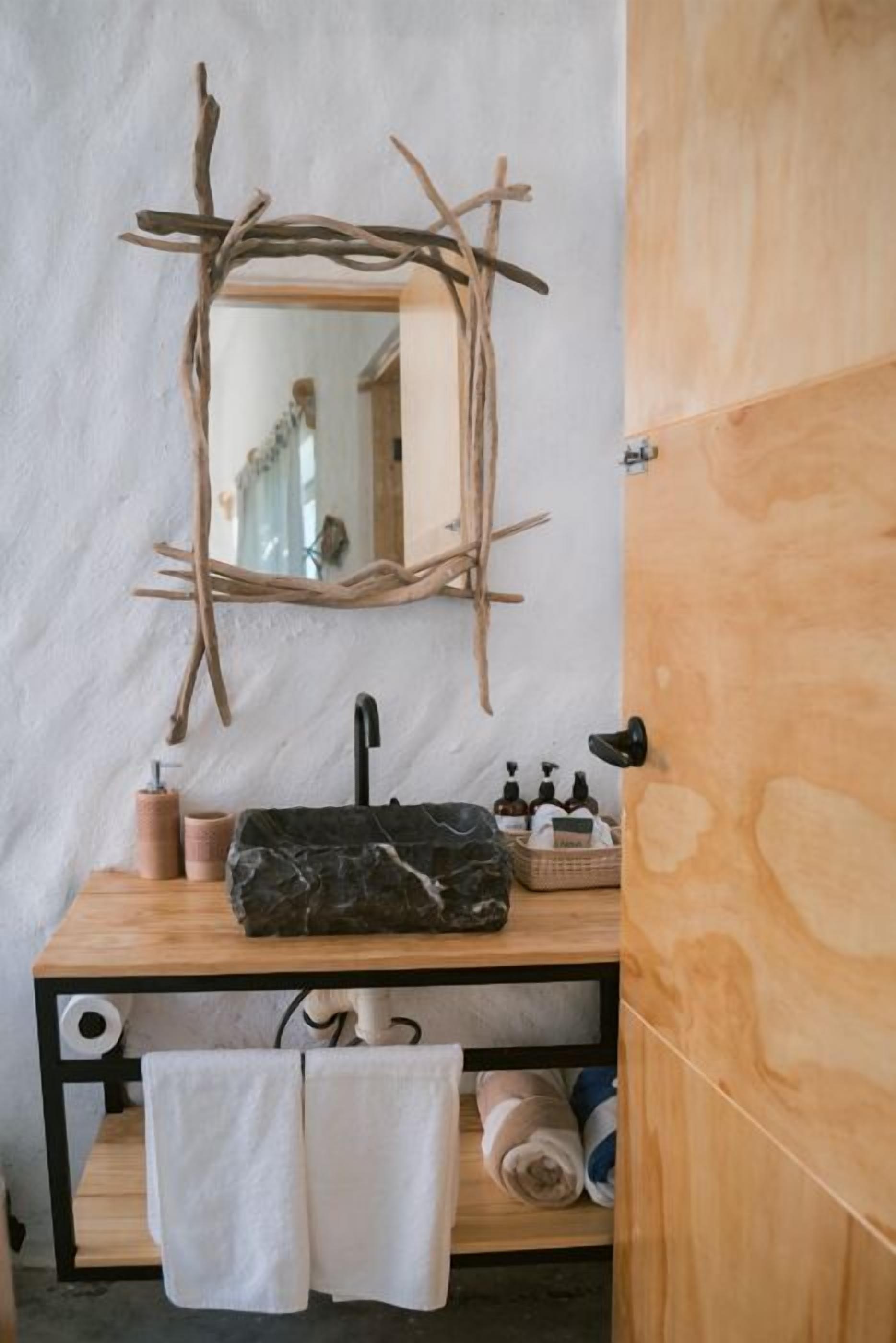 A bathroom with a wooden vanity, a mirror with a branch frame, a black faucet, and towels.