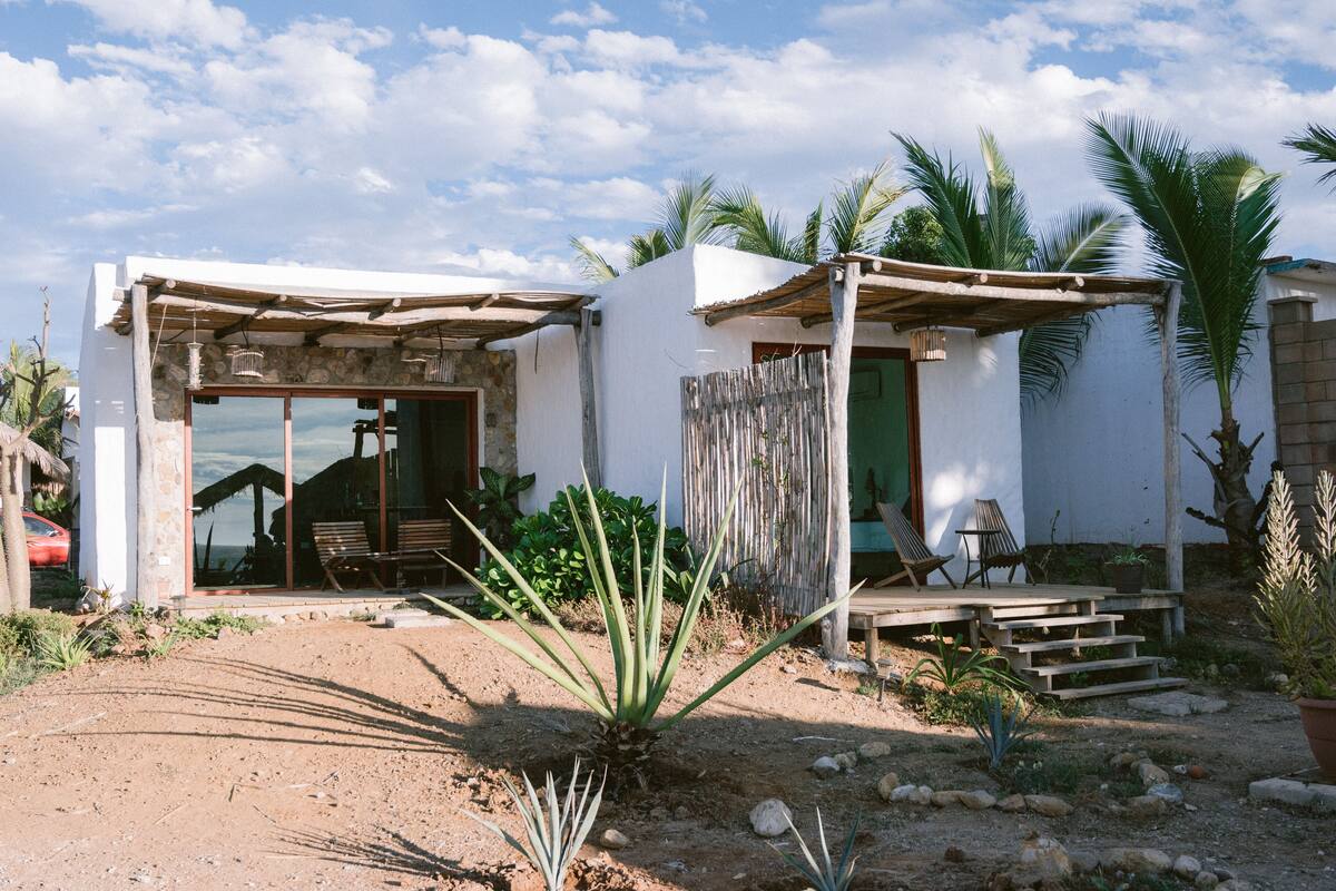 Una casa pequeña y rústica con un patio, que incluye una terraza de madera y una zona de estar con sillas.