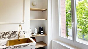 Une cuisine dotée d’un plan de travail en marbre, d’un évier doré et d’une fenêtre donnant sur la verdure.