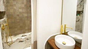 Une salle de bain moderne avec une douche en marbre, un lavabo blanc et un grand miroir.