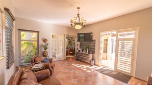 A spacious living area with a brown leather sofa, a chandelier, and a view of the outdoors through large sliding doors. - CASA CANAVERAL-TropicalPrivatePool-14Family-sized! Near Rafael Hernandez Airport (Isabela)