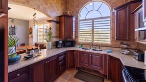 A kitchen with dark wooden cabinets, a granite countertop, a large window with blinds, and a hanging light fixture. - CASA CANAVERAL-TropicalPrivatePool-14Family-sized! Near Rafael Hernandez Airport (Isabela)