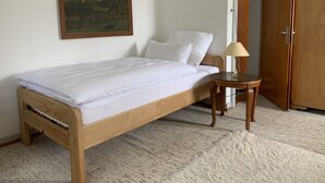 A bedroom with a wooden bed, white bedding, a small round table with a lamp, a painting on the wall, and a wooden wardrobe. - Garten, Thermomix und Babybett (Ühlingen-Birkendorf)