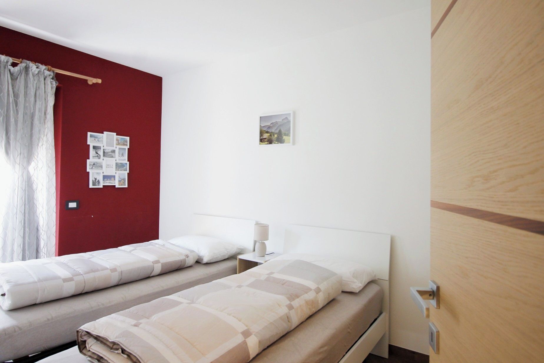 Een hotelkamer met twee bedden, een rode accentmuur, een klein prentje en een houten garderobe.