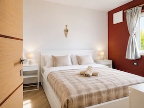 Une chambre à coucher avec un lit, des tables de chevet avec des lampes, un luminaire fixé au mur et une fenêtre avec des rideaux.