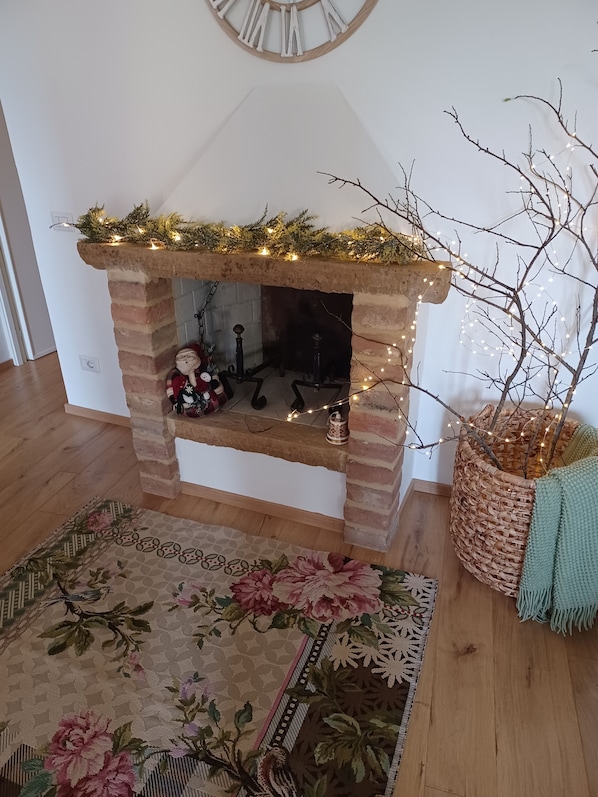 En tegelbeklädd öppen spis dekorerad med en ljusslinga, en blommönstrad matta och en flätad korg med en gren i.