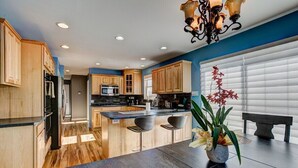 Une cuisine moderne avec des meubles en bois, un îlot central doté de tabourets, un lustre et une plante en pot.
