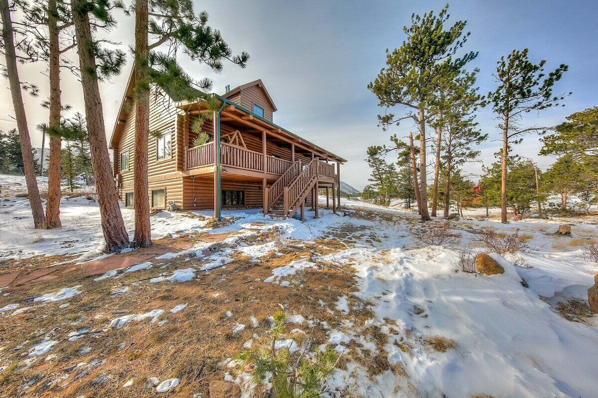A wooden cabin with a balcony, surrounded by trees and snow.