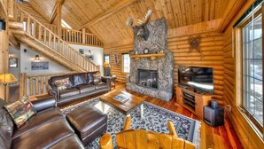 A log cabin interior with a stone fireplace, leather furniture, a staircase, and a television. - Moose Mountain Lodge - Secluded Log Home w/Beautiful Mountain Views (Estes Park)
