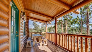 A wooden deck with a bench and a table, surrounded by a railing, overlooking a forested area. - Moose Mountain Lodge - Secluded Log Home w/Beautiful Mountain Views (Estes Park)