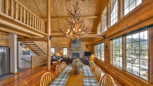 A log cabin interior with a dining area, fireplace, and large windows. - Moose Mountain Lodge - Secluded Log Home w/Beautiful Mountain Views (Estes Park)