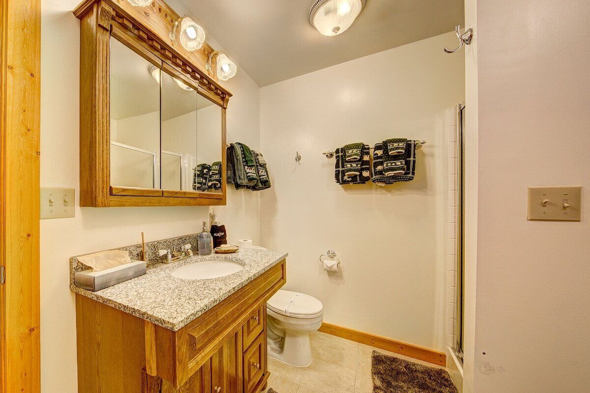 A bathroom with a wooden vanity, a large mirror, a sink, a toilet, and a shower.