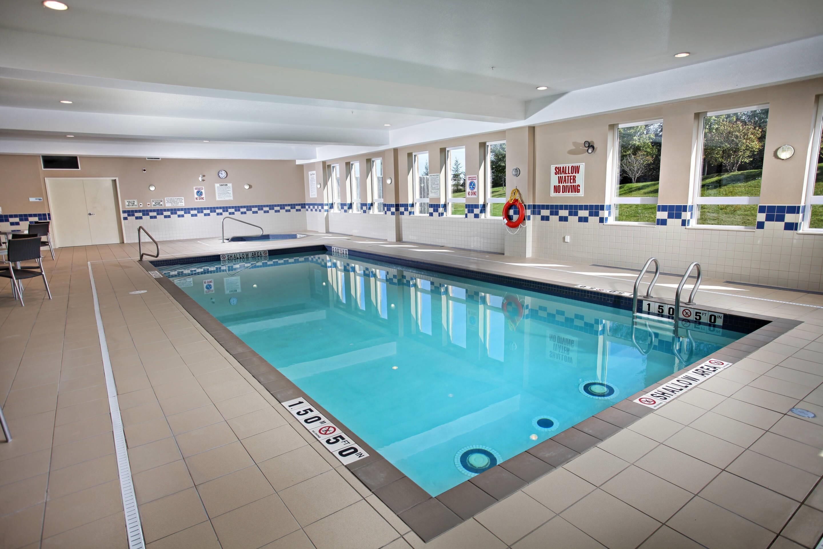 An indoor swimming pool with clear water, marked depth lines, and safety signs.
