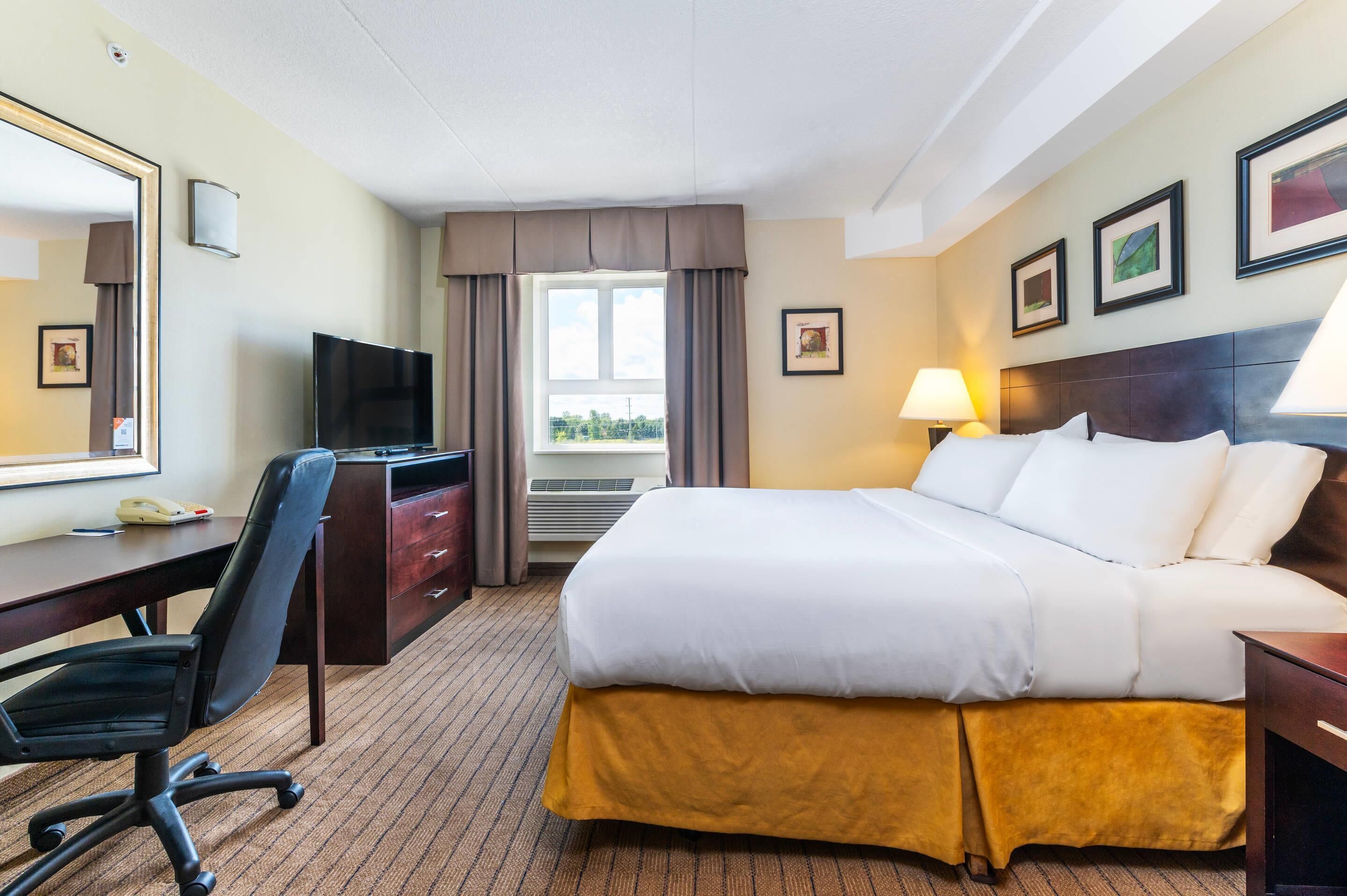 A hotel room with a bed, desk, chair, television, and window with curtains.